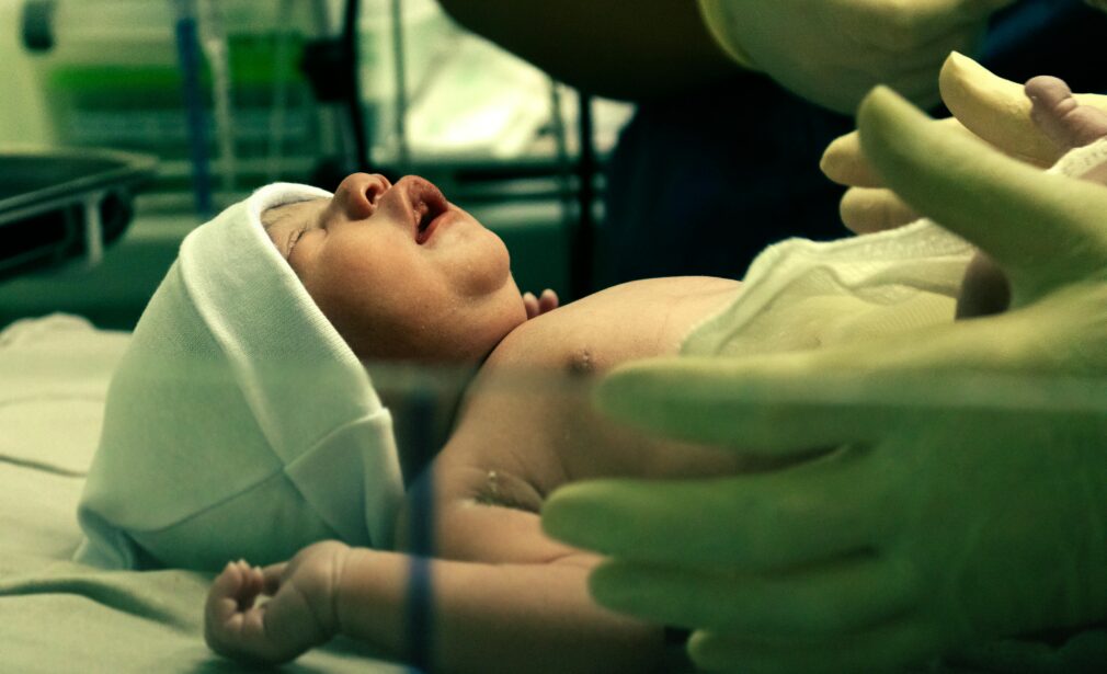 A newborn baby being gently handled by a nurse in a hospital setting.