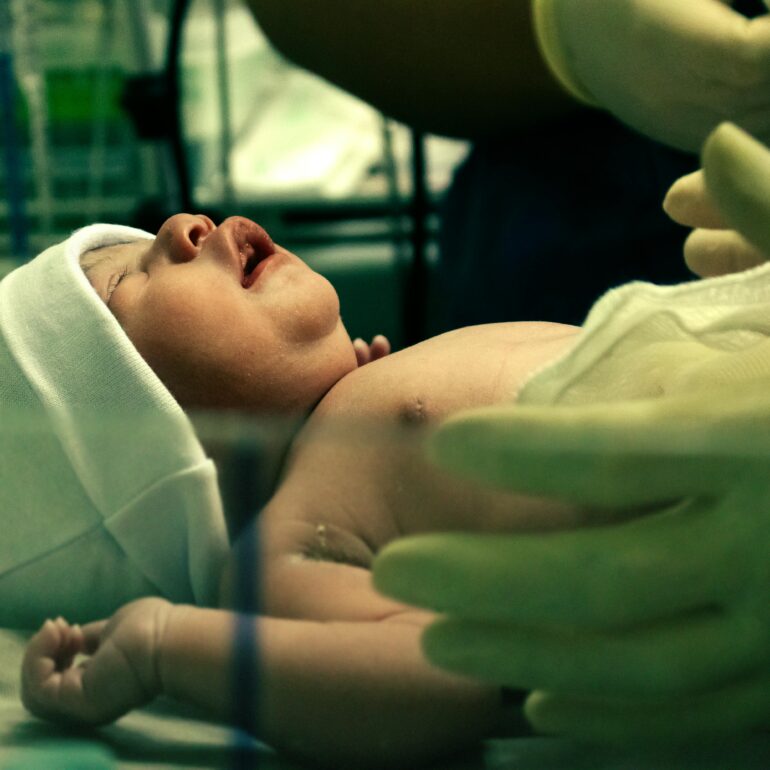 A newborn baby being gently handled by a nurse in a hospital setting.