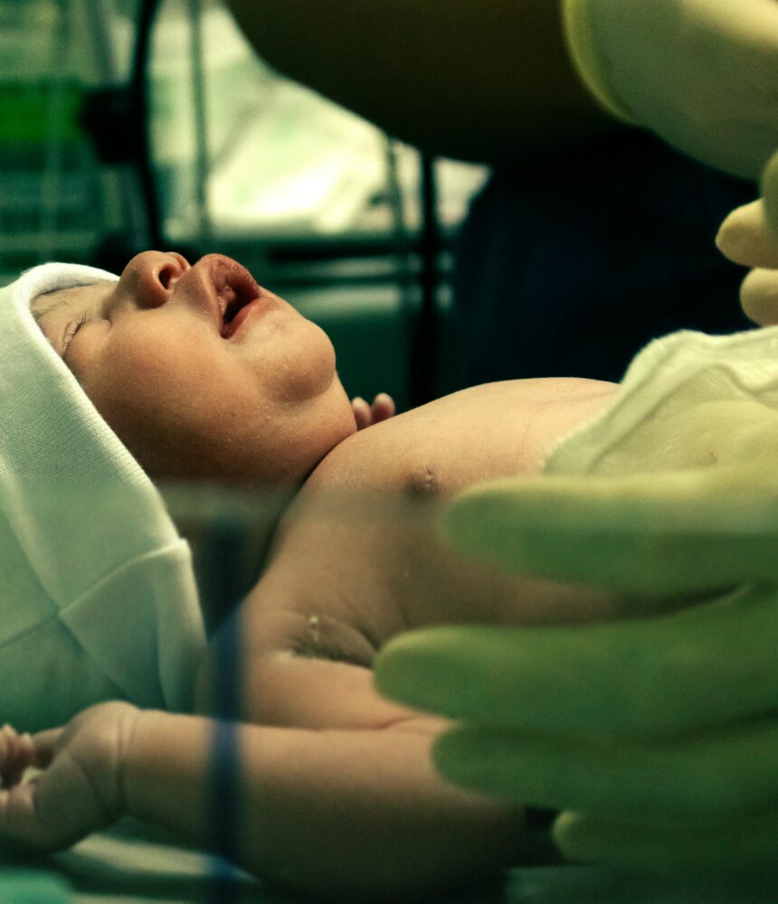 A newborn baby being gently handled by a nurse in a hospital setting.