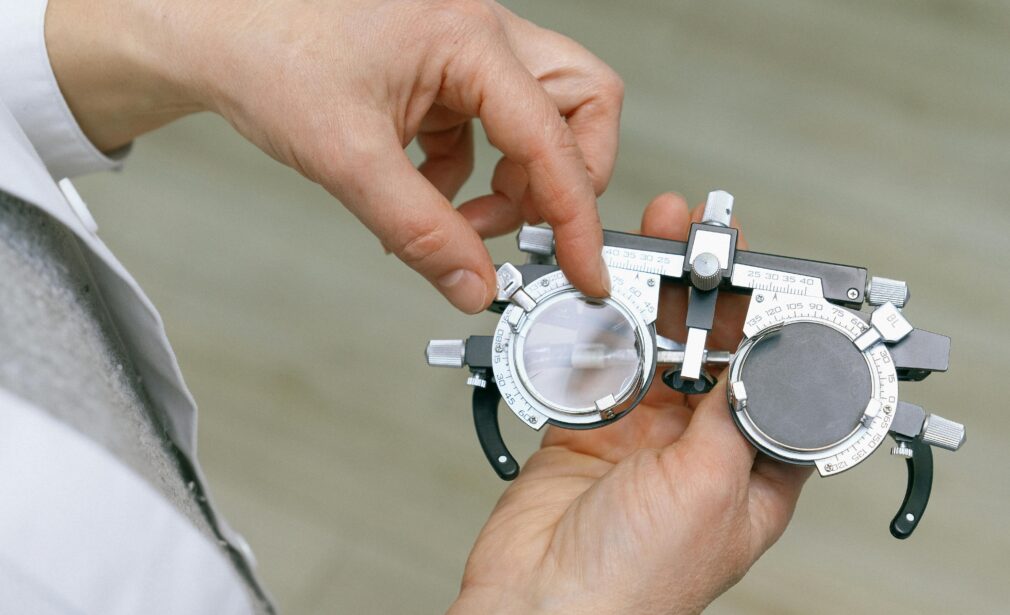 Crop unrecognizable medic in white coat taking measuring vision glasses while adjusting scale according to numerals written on metal surface