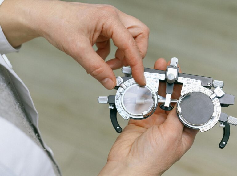 Crop unrecognizable medic in white coat taking measuring vision glasses while adjusting scale according to numerals written on metal surface