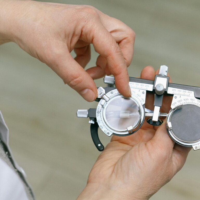 Crop unrecognizable medic in white coat taking measuring vision glasses while adjusting scale according to numerals written on metal surface