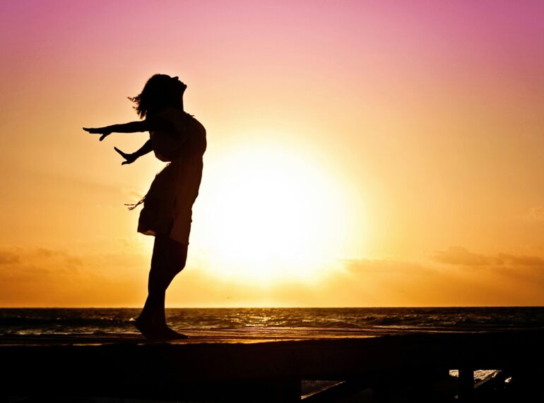 Silhouette of a woman at the beach with arms outstretched against a vibrant sunset backdrop.