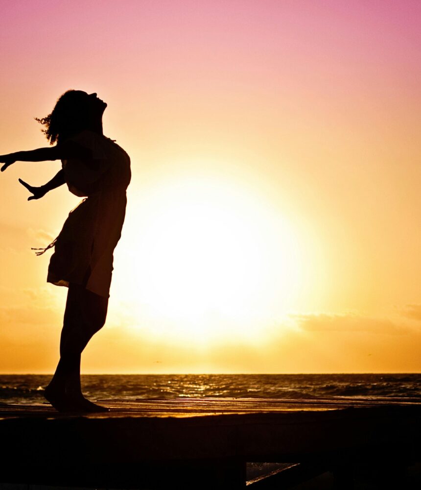 Silhouette of a woman at the beach with arms outstretched against a vibrant sunset backdrop.